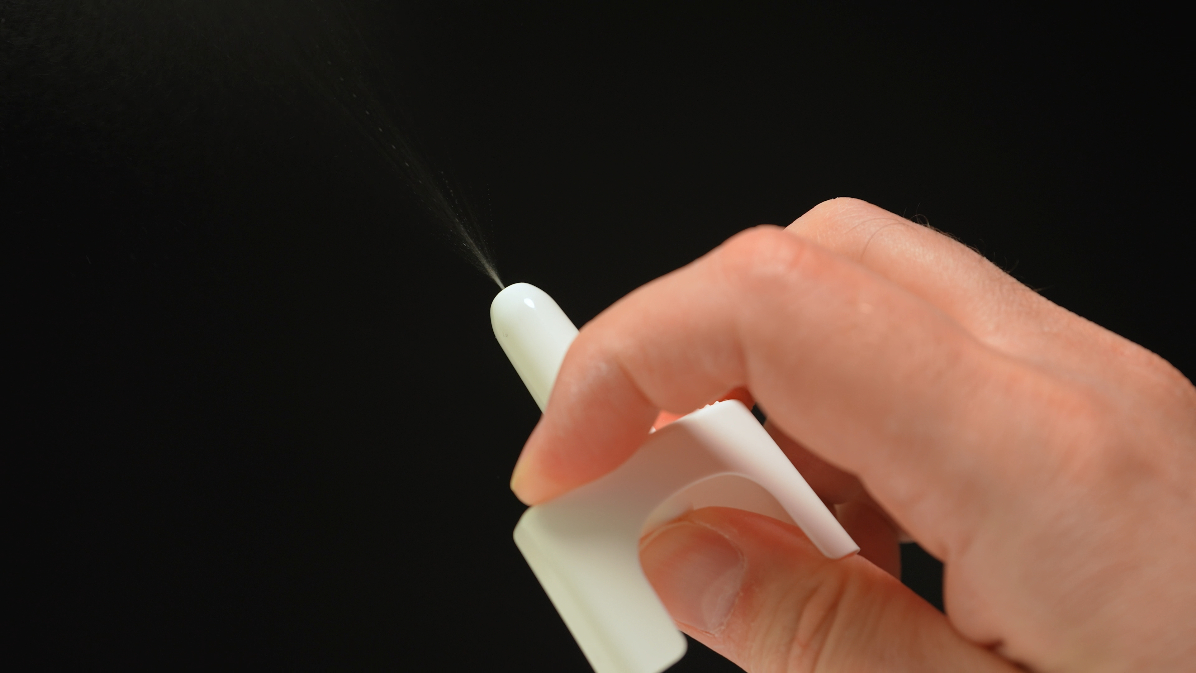 A hand holds a naloxone container and is spraying it. Black background.